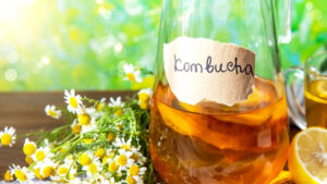 glass bottle filled with combucha with some chamomile on the side