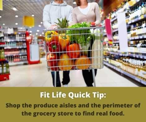 Man and woman walking through supermarket with basket full of vegetables and fruits