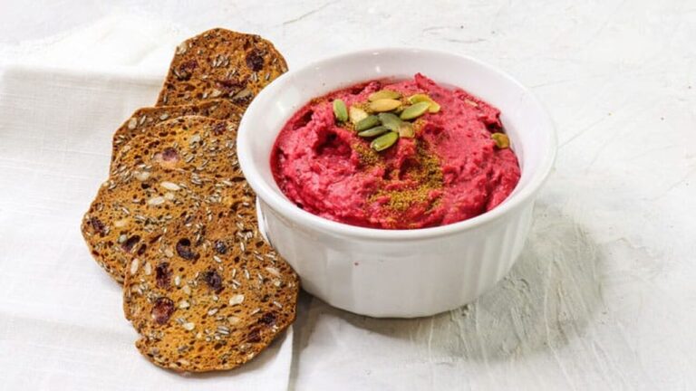 beet hummus served in a small white bowl, and some whole seed crackers on the side