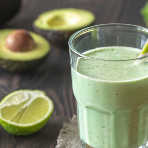 Glass full of green smoothie, avocado and limes on the side