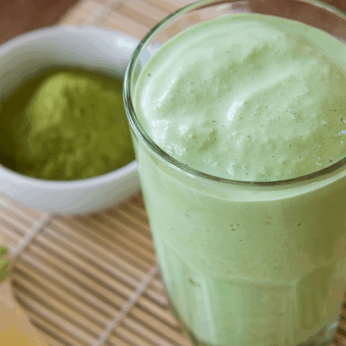 green smoothie served in a glass and small bowl full of matcha powder on the side
