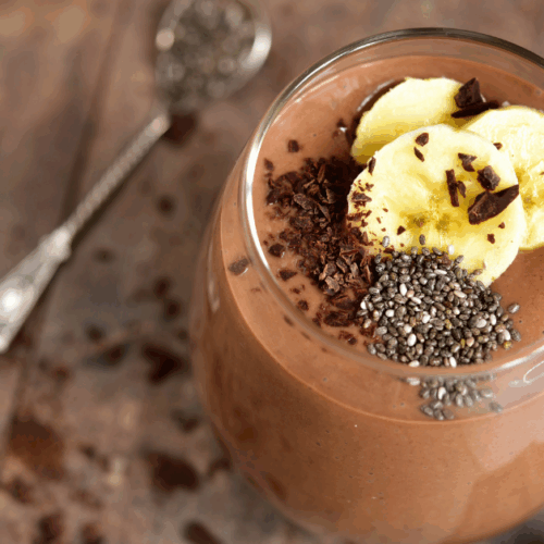 Glass full of brown smoothie toped with banana slices and chia seeds