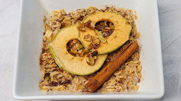 Oatmeal served in a white bowl topped with cinnamon stick and dried apple rings