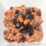 oatmeal served in a white bowl topped with chocolate chips, dried cherries, and almonds