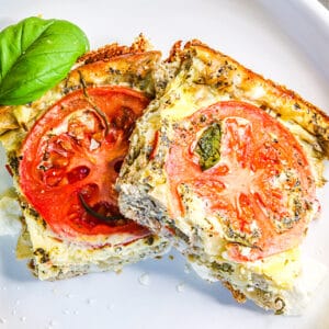 Two pieces of casserole served on a white plate, and some fresh basil leaves on the side