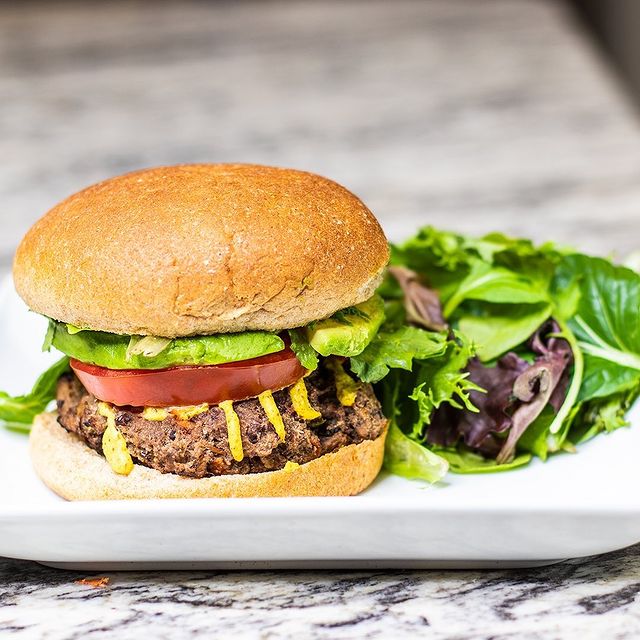 burger served on a white plate with some greens on the side